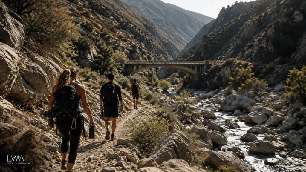 Hikers following a rocky canyon trail toward a remote bridge before a California bungee jumping adventure.