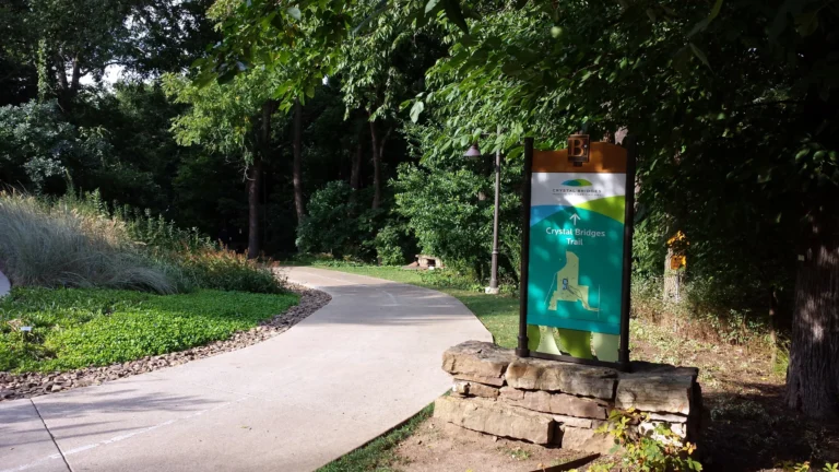 A paved path curving through trees beside a sign for Crystal Bridges Trail.