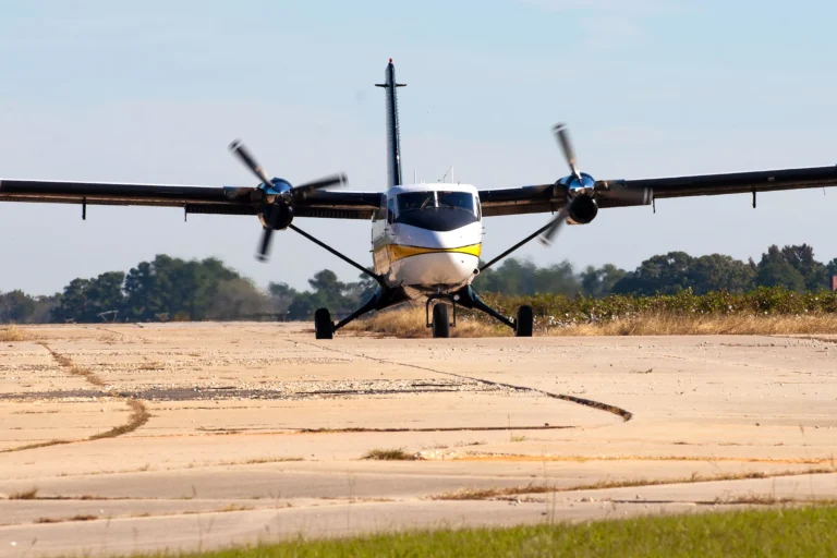 A twin-engine propeller aircraft facing the camera on an airfield, with its propellers turning.